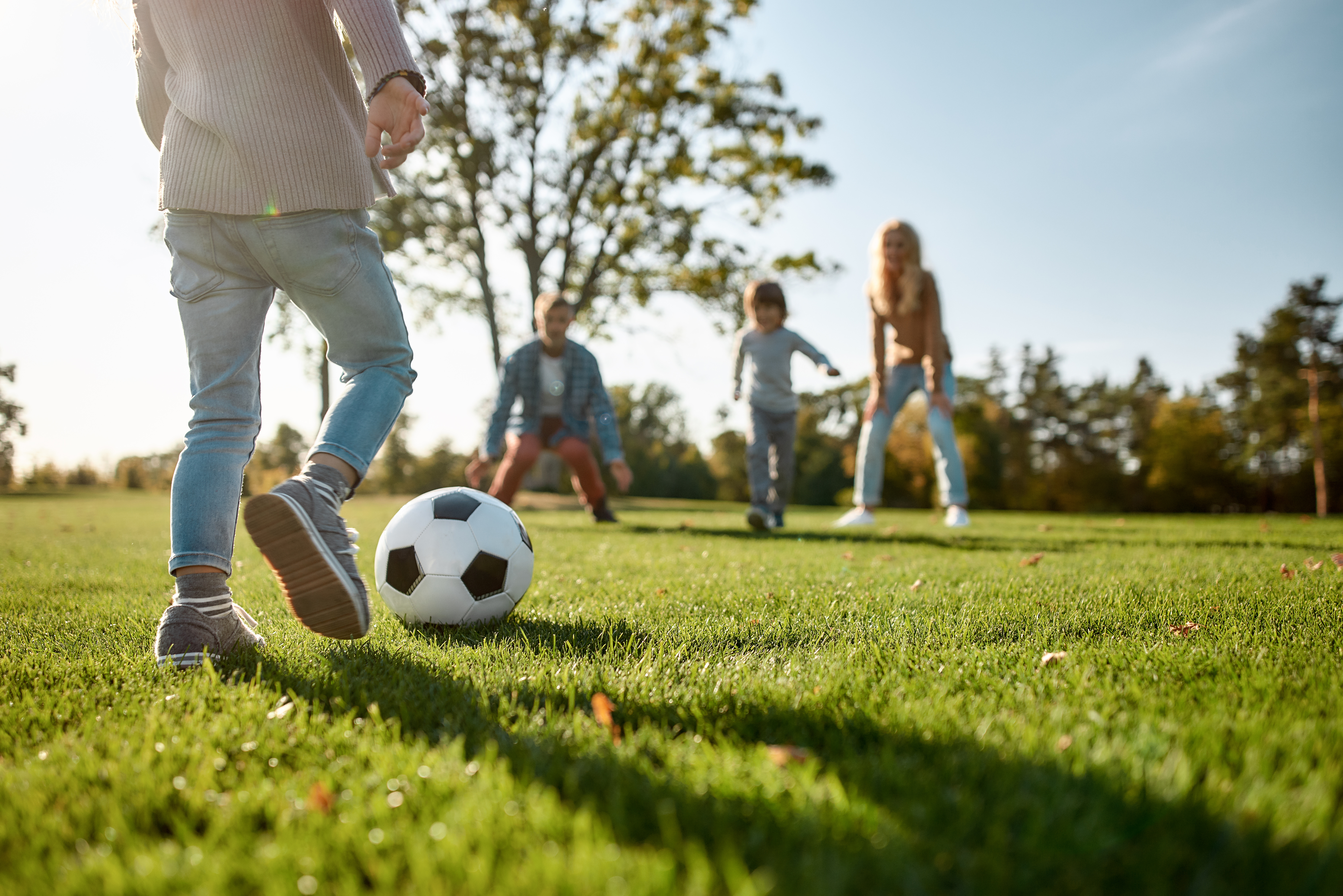Cropped portrait of cheerful little girl playing football with her family in the park on a sunny day. She is having fun while running the ball. Family, kids and nature concept. Horizontal shot.