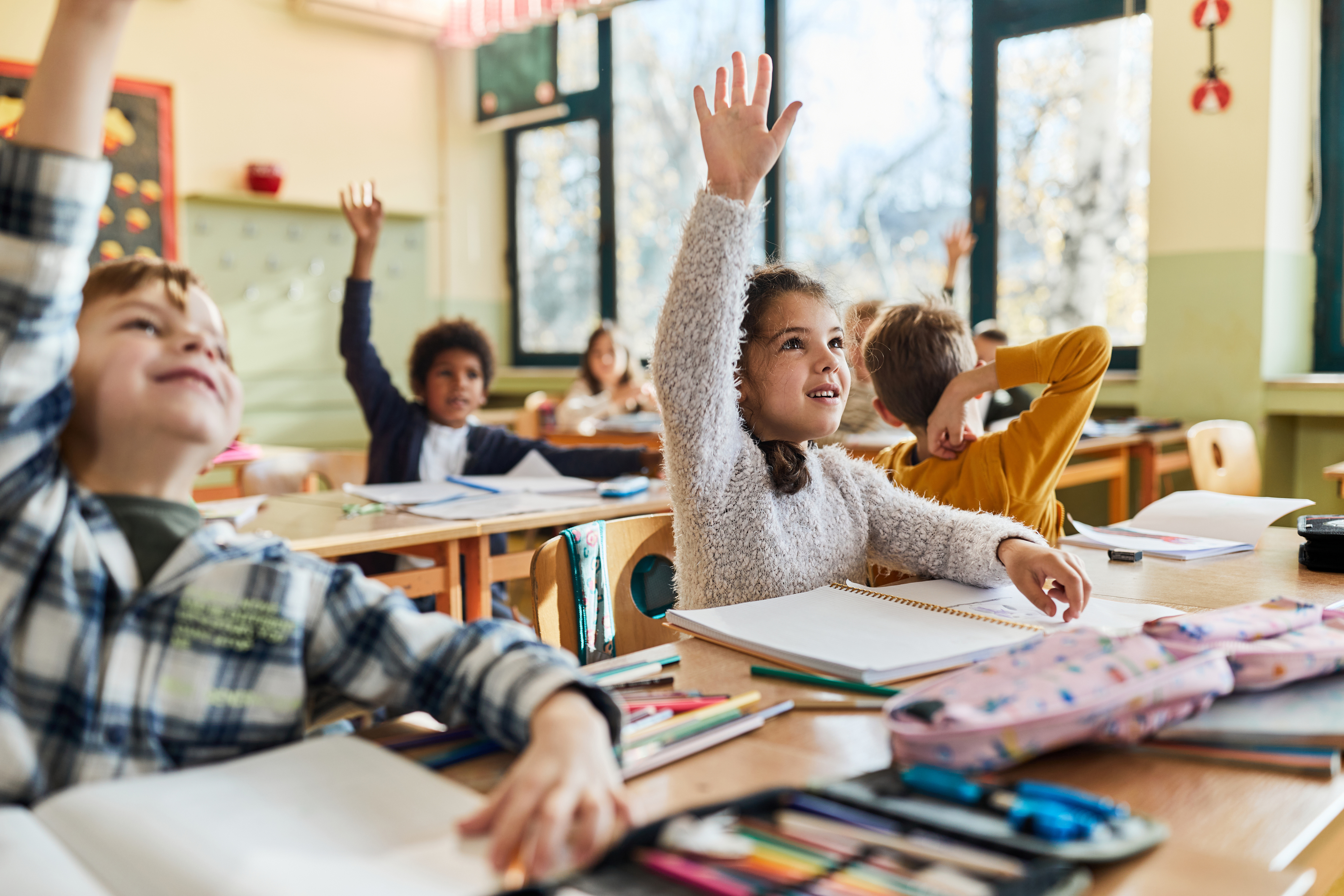 Happy elementary students raising their hands on a class at school. Focus is on girl.