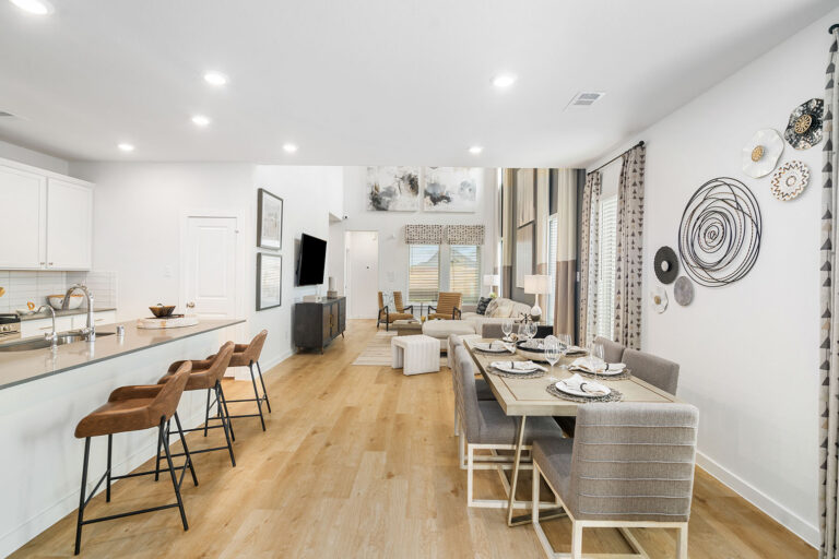 Open-concept kitchen and dining area with white cabinetry, large island seating, modern décor, and light wood flooring in a new construction home