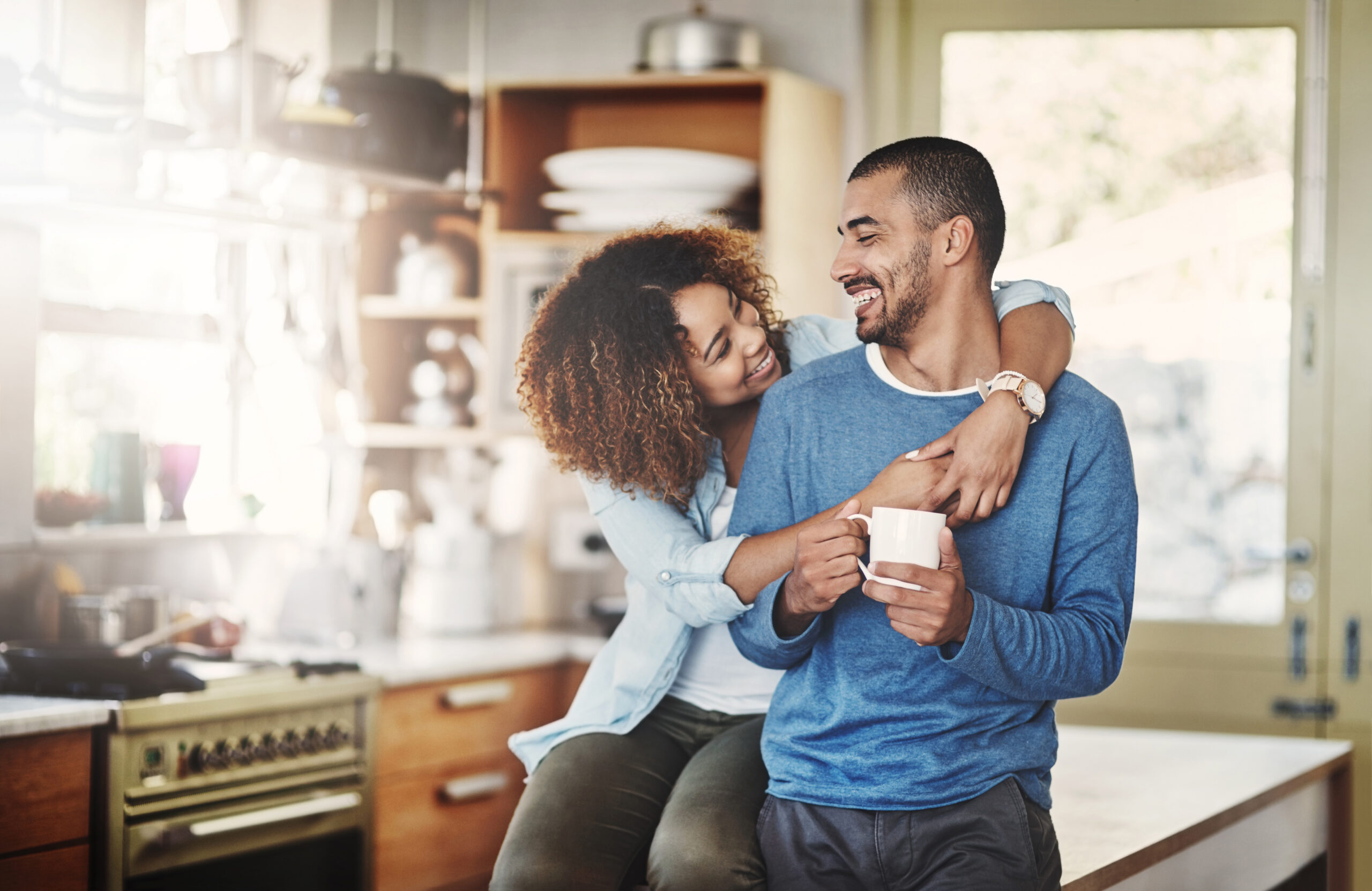 Love, coffee and happy couple in kitchen, morning hug in home with smile, hugging and healthy relationship. Happiness, man and woman embrace with affection, romance and young people in apartment