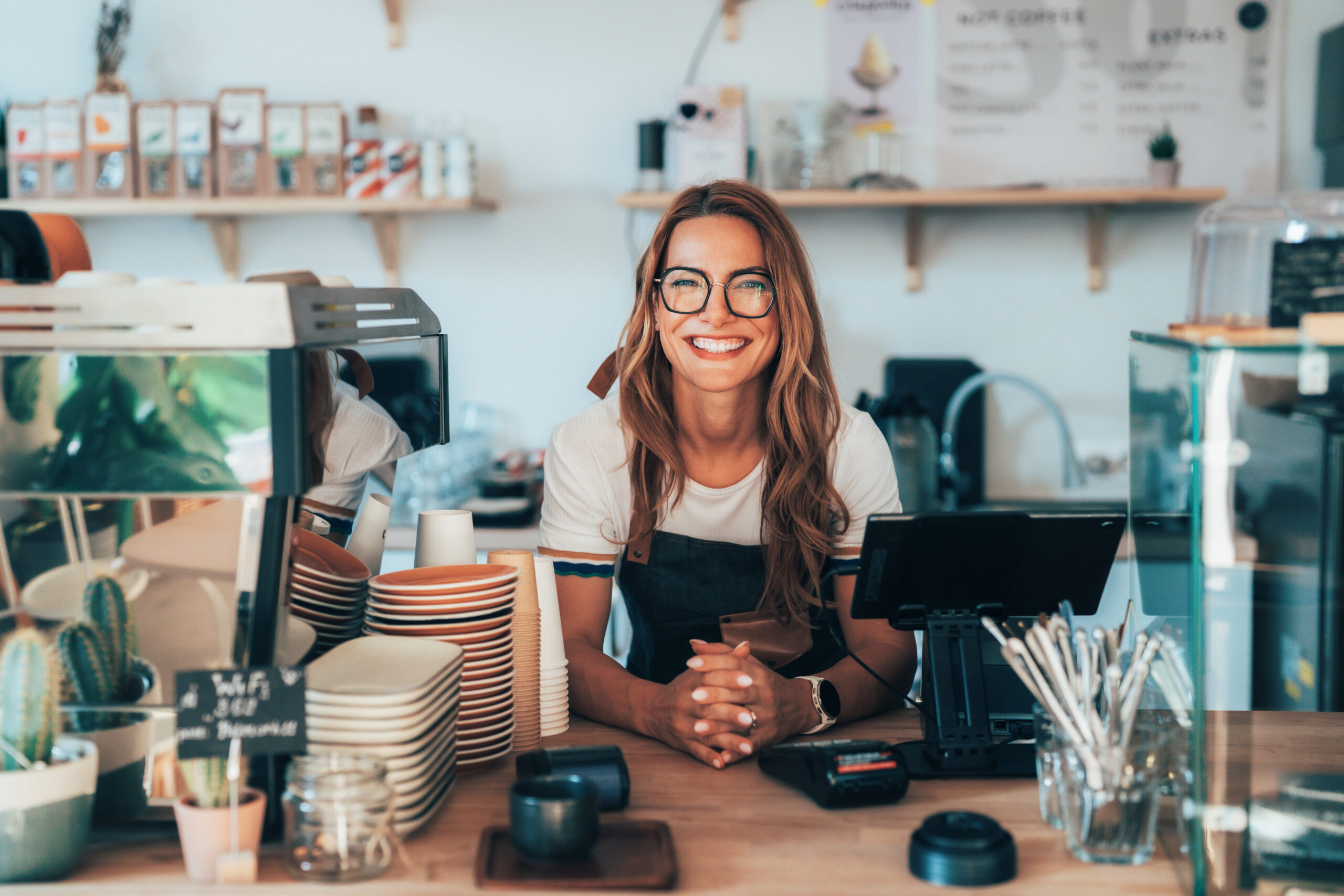Portrait of young woman standing at the counter in her cafe. Coffee shop owner in apron smiling at camera